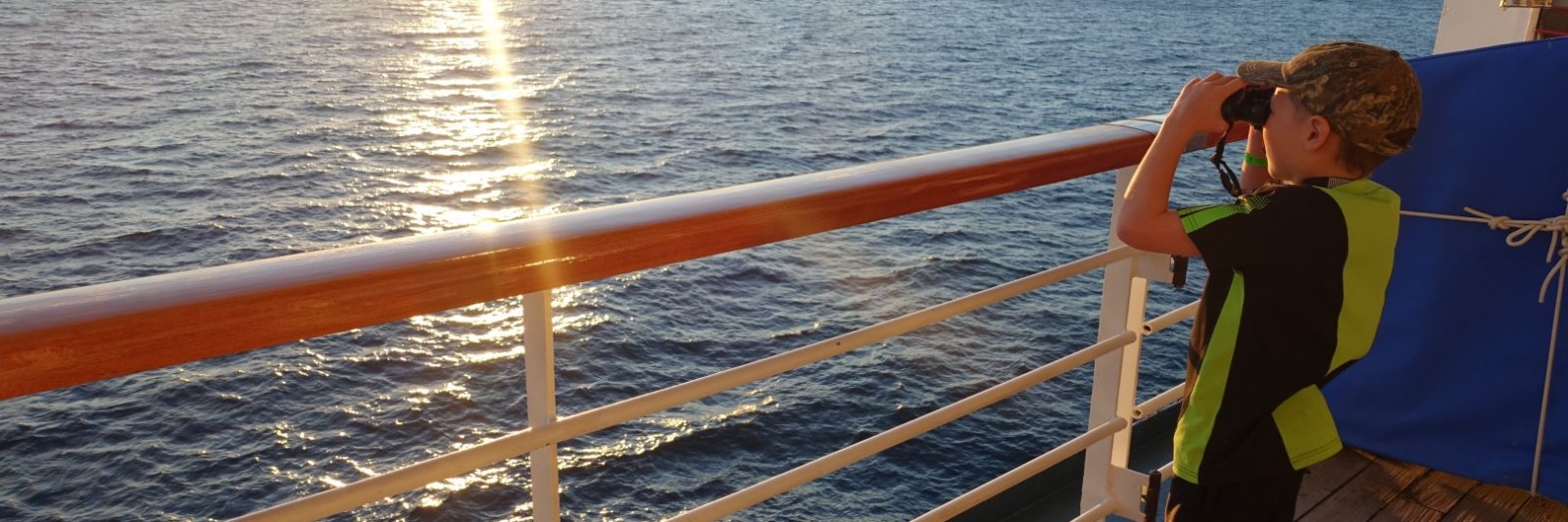 Boy looking into the ocean through binoculars from cruise ship