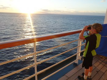 Boy looking into the ocean through binoculars from cruise ship