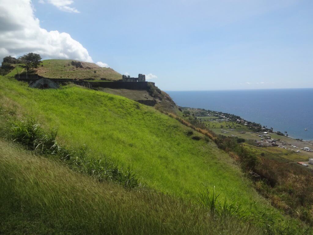 grassy hill with ocean and fortress in the background