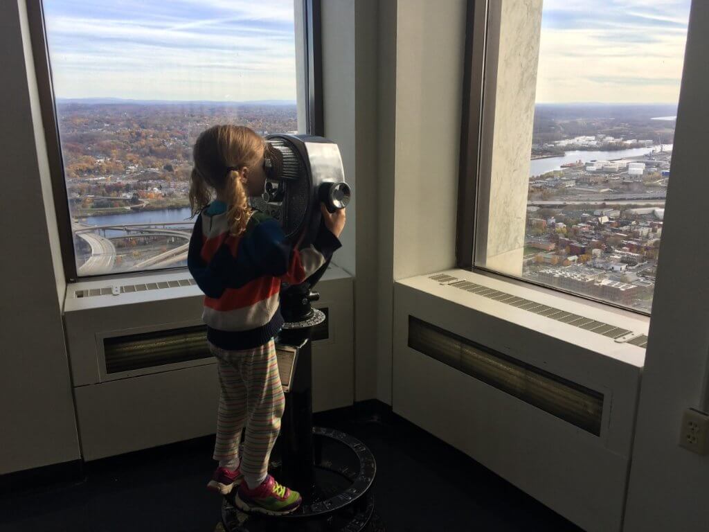 girl looking through binoculars at city through windows