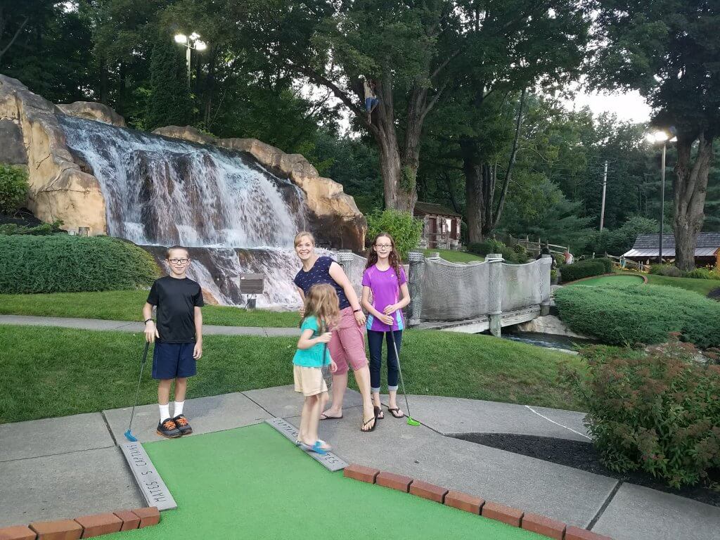 mom and kids playing mini golf with waterfall background