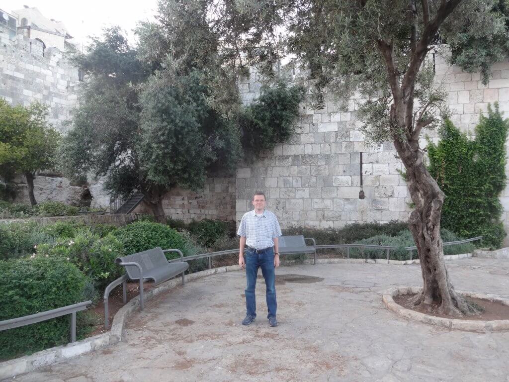 man in front of stone wall with green trees and bushes