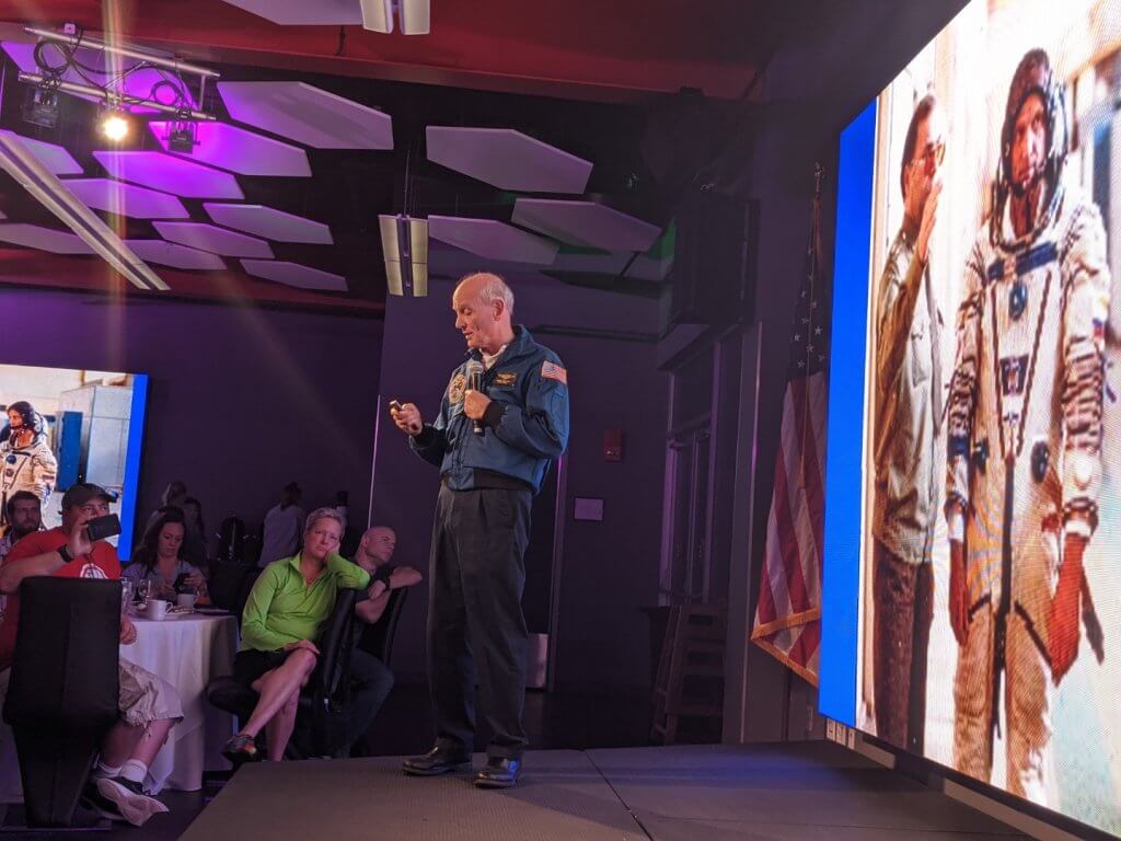 man speaking in front of large screen