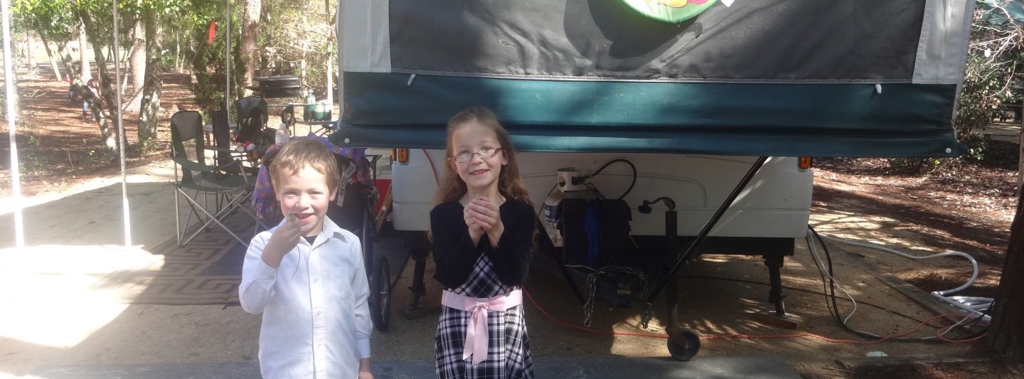 boy and girl holding lizards in front of camper trailer