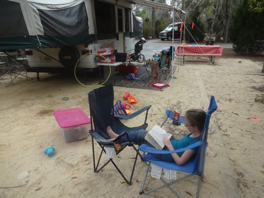 girl reading on a camp chair with pop-up trailer