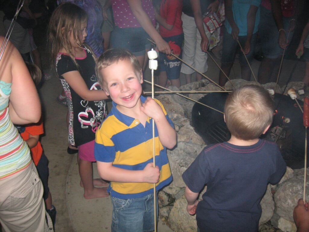 boy with marshmallows on a stick at campfire with others around