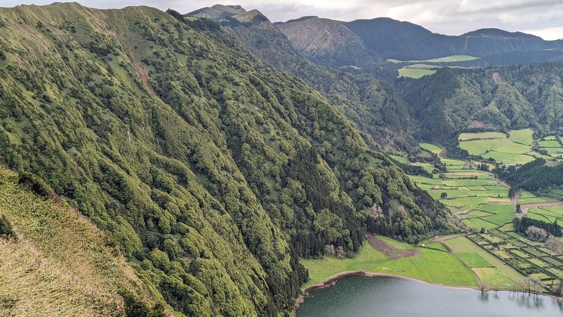 steep green mountainside with lake below